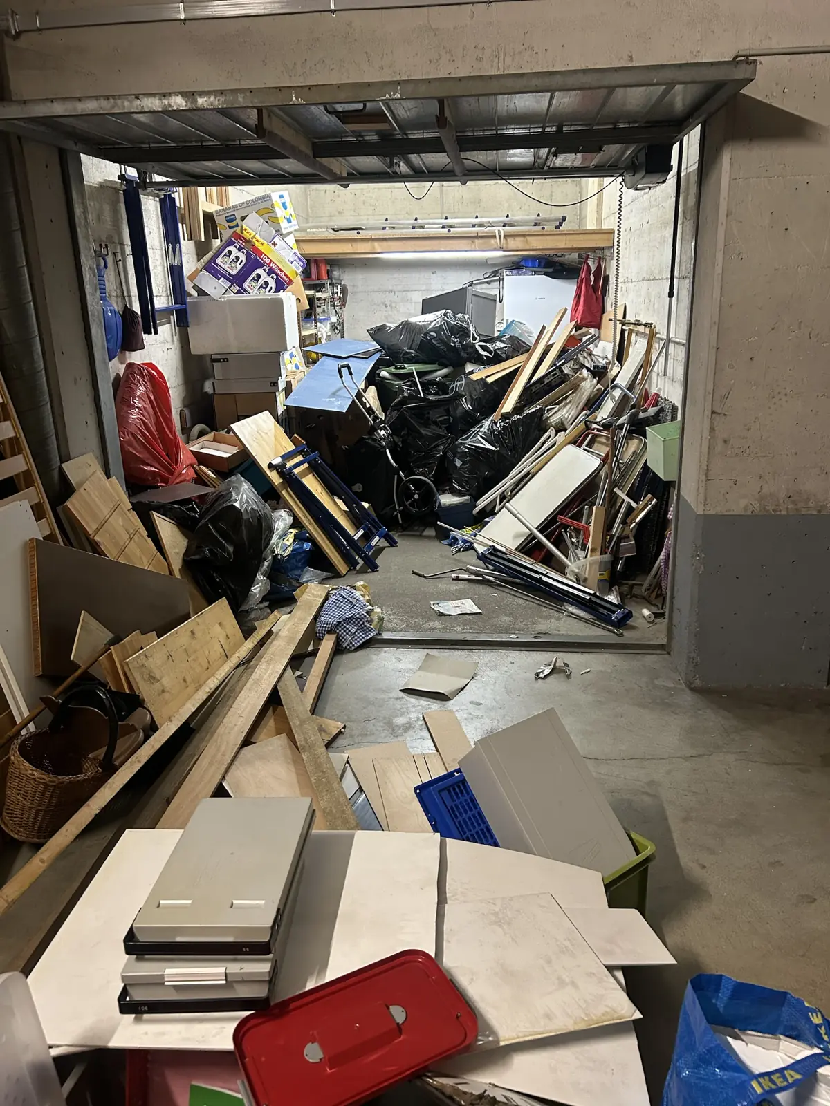Garage en sous-sol encombré de planches, sacs et outils avant débarras, région de Fribourg